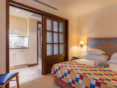 Camera d'hotel con letto singolo con biancheria colorata e cucina adiacente tramite porta scorrevole in vetro