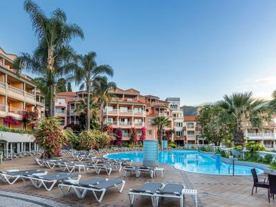 Complesso alberghiero con piscina circondata da lettini e palme sotto un cielo limpido.