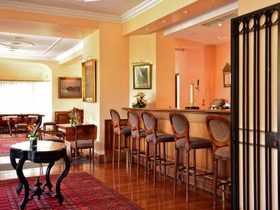 Elegante bar dell'hotel con sgabelli in legno, tappeto e area salotto con divani e tavoli.