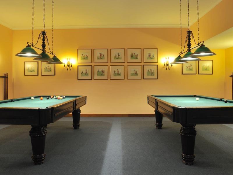 Due tavoli da biliardo in una stanza illuminata soffusamente con colori caldi e quadri incorniciati alla parete.