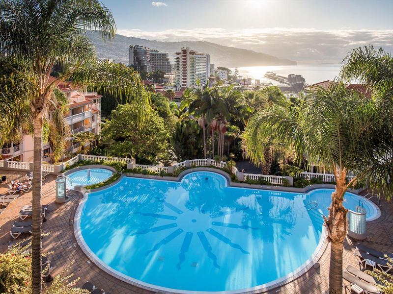 Piscina con disegno solare in giardino tropicale con vista sul mare e sulla città.