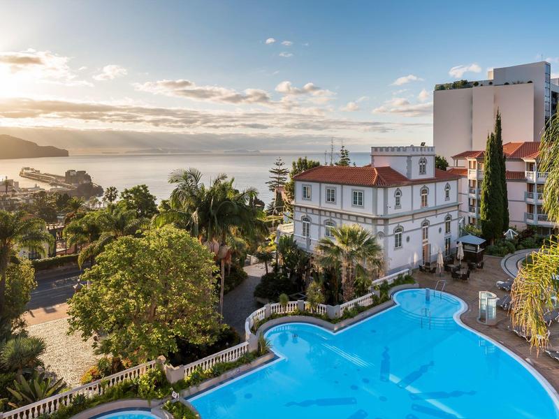Hotel con grande piscina all'aperto, giardino e vista sulla costa al tramonto.