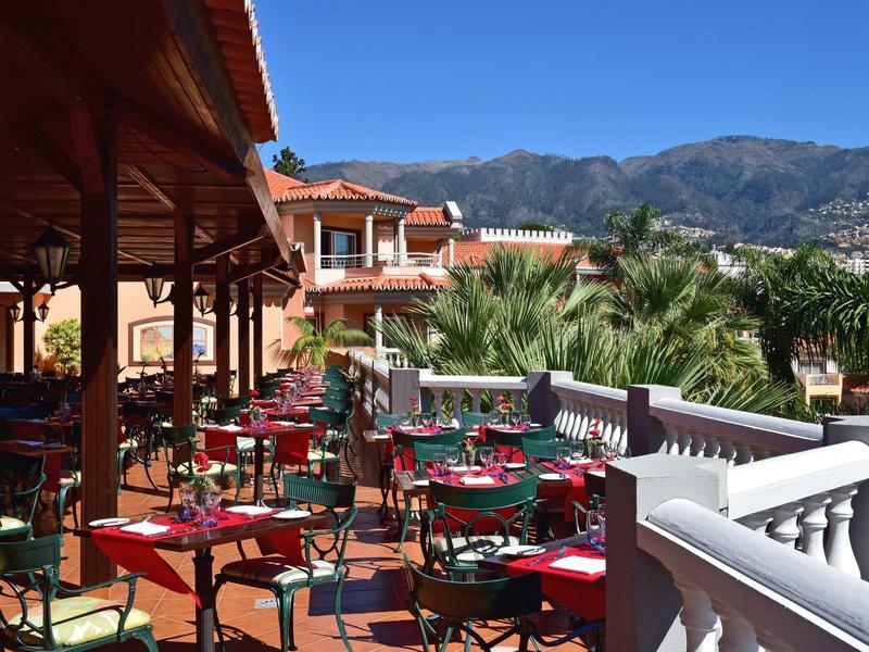 Terrazza di hotel con tavoli apparecchiati, sedie e vista su montagne e palme.