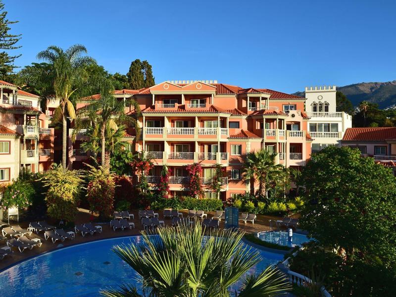 Hotel multi-piano circondato da palme e piscina con tempo soleggiato.
