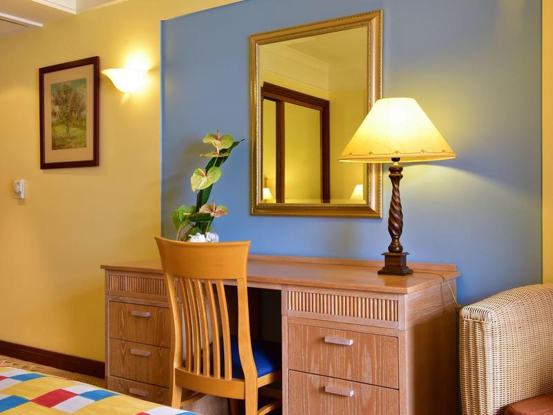 Scrivania con sedia, lampada e pianta davanti a una parete blu in una camera d'hotel.