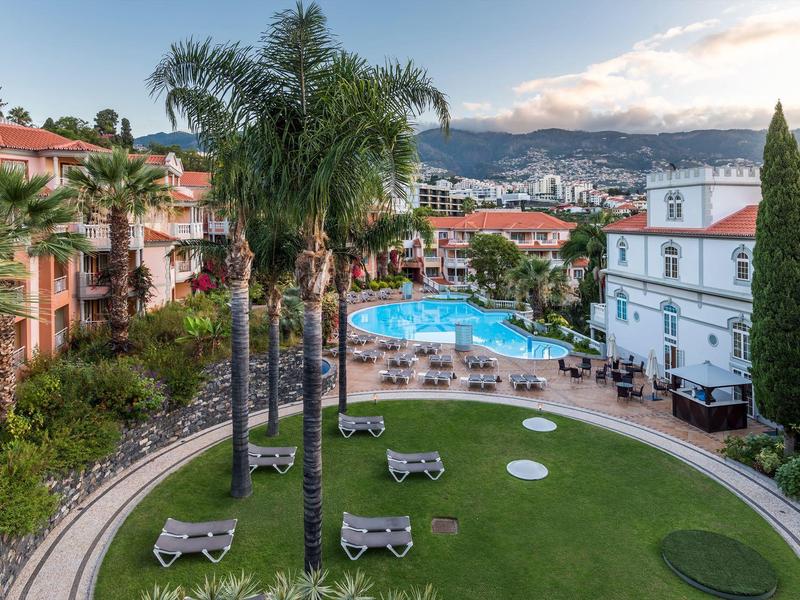 Vista su un giardino dell'hotel con palme, sdraio e una grande piscina.