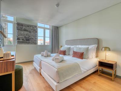 Nowoczesny pokój hotelowy z podwójnym łóżkiem, drewnianą podłogą i dużymi oknami.