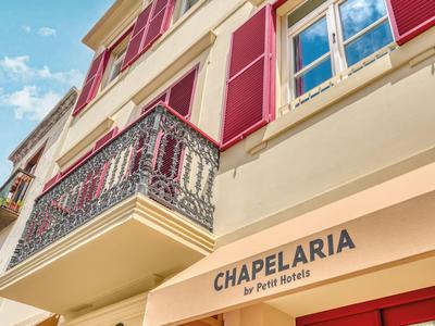 Jasna, elegancka fasada hotelu z czerwonymi okiennicami i ozdobnym balkonem pod niebieskim niebem.