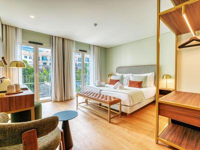Przestronny pokój hotelowy z łóżkiem podwójnym, drewnianymi meblami i dużymi oknami z widokiem na zewnątrz.