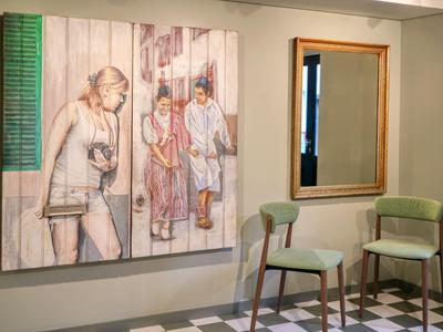 Poczekalnia hotelowa z dwoma zielonymi krzesłami, lustrem i dziełem sztuki na ścianie.