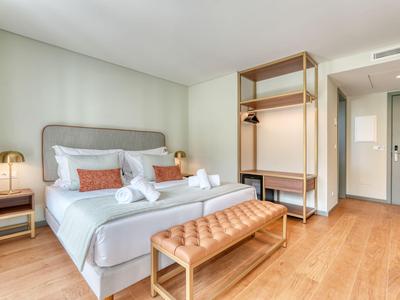 Jasny pokój hotelowy z podwójnym łóżkiem, drewnianą podłogą i nowoczesnym wyposażeniem.