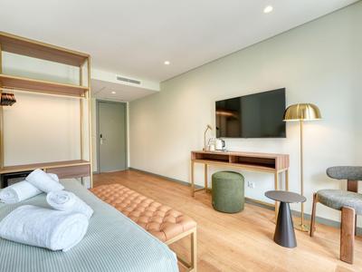 Nowoczesny pokój hotelowy z łóżkiem, telewizorem i miejscem do siedzenia na drewnianej podłodze.