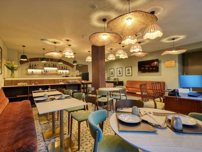 Przytulny bar hotelowy z stołami, krzesłami i ciepłym oświetleniem.