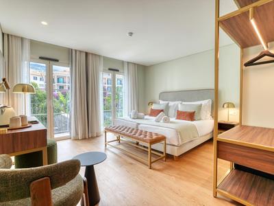 Jasny pokój hotelowy z łóżkiem podwójnym, częścią wypoczynkową i dużymi oknami z widokiem na park.
