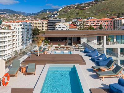 Piscina moderna de hotel con tumbonas en la terraza de la azotea y vistas a la montaña al fondo.