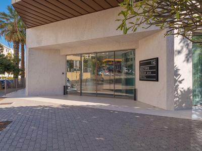 Entrada moderna de hotel con grandes ventanas de vidrio, sol y un camino pavimentado.