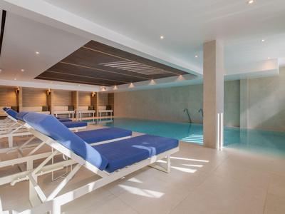 Piscina cubierta moderna con tumbonas azules e iluminación indirecta.