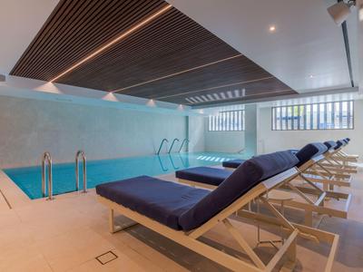Piscina interior moderna con tumbonas azules y techo de madera en un hotel.