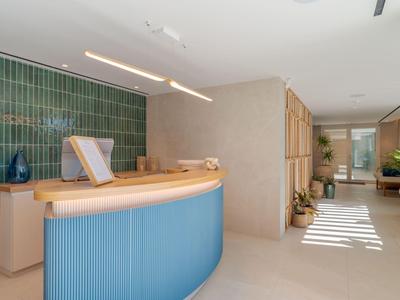 Recepción moderna de hotel con mostrador azul y pared de azulejos verdes.