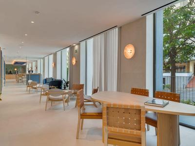 Moderna sala de hotel con sillas de madera, mesas y grandes ventanas con vista al jardín.