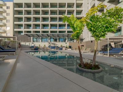 Piscina moderna de hotel con tumbonas y plantas frente a un edificio de varios pisos.