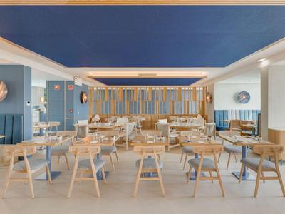 Área de comedor luminosa y moderna con muebles de madera y techo azul en un hotel.