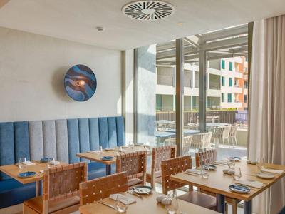 Restaurante de hotel modernamente amueblado con mesas preparadas y grandes ventanales.