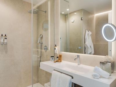 Nowoczesna łazienka hotelowa z dużym prysznicem, podwójnymi umywalkami i dobrze oświetlonym lustrem.