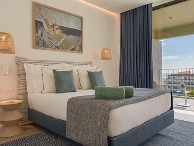 Nowoczesny pokój hotelowy z dużym łóżkiem, dekoracją ścienną i balkonem z widokiem na wodę.