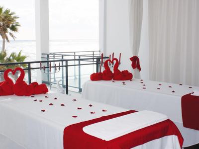 Zwei Massageliegen mit roten Handtüchern und Rosenblättern vor einer Balkonbrüstung mit Meerblick.