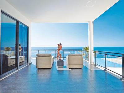 Moderner Balkon mit Glasgeländer, Sitzmöbeln und Meerblick bei klarem Himmel.