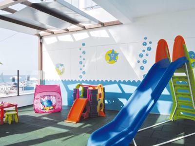 Helle Indoor-Spielbereich mit blauem Rutsche, buntem Klettergerüst und Fenstern für Sonneneinfall.