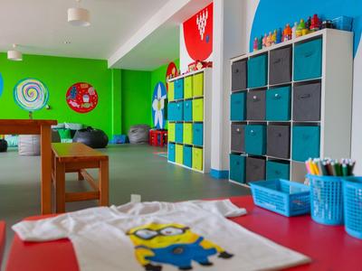 Kindergartenraum mit bunten Möbeln, Spielecken, bunten Wänden und einem Tisch mit Malutensilien.