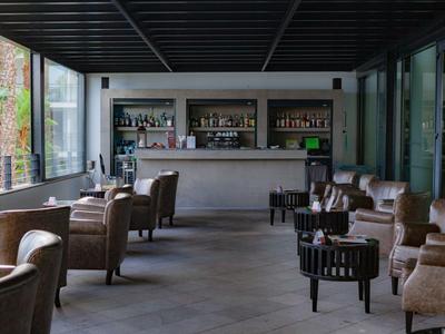 Moderner Lounge-Bereich mit braunen Sesseln, schwarzen Tischen und einer Bar im Hintergrund.