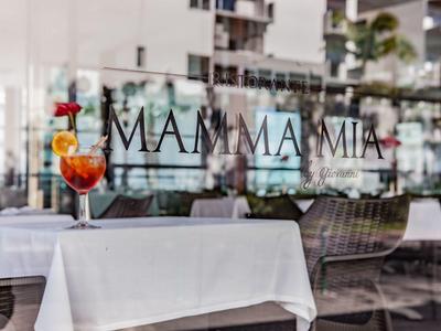 Restaurantterrasse mit weißen Tischtüchern, Weinglas mit Dekoration und Schriftzug "MAMMA MIA".