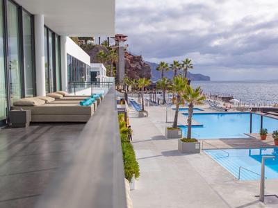 Moderner Außenbereich mit Lounge-Möbeln, Pool, Palmen und Meerblick unter bewölktem Himmel.