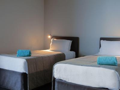 Zwei Einzelbetten mit weißen Laken und blauen Handtüchern in schlichtem, modernem Schlafzimmer.