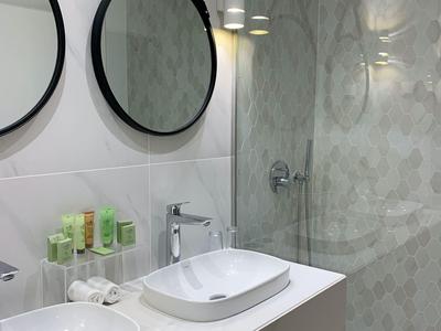 Modernes Badezimmer mit zwei weißen Waschtischen, runden Spiegeln und einer begehbaren Dusche.