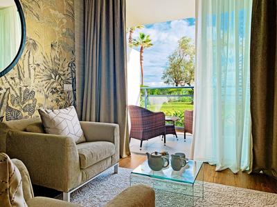 Gemütliches Wohnzimmer mit braunem Sessel, Glastisch und Blick auf Terrasse mit Stühlen und Pflanzen.
