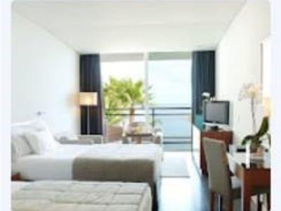 Modernes Hotelzimmer mit zwei Betten, Schreibtisch, Fernseher und Balkon mit Meeresblick.