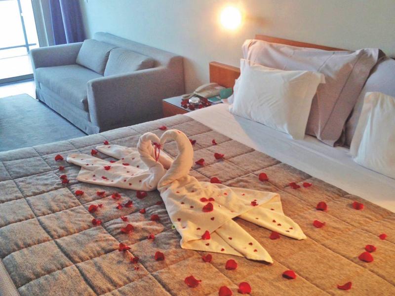 Camera d'hotel con letto decorato con asciugamani a forma di cigni e petali di rosa.
