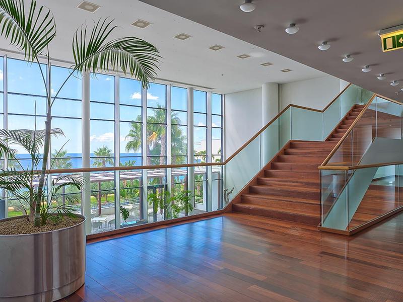 Luminoso corridoio d'hotel con grande finestra, scala, pavimento in legno e piante in vaso.