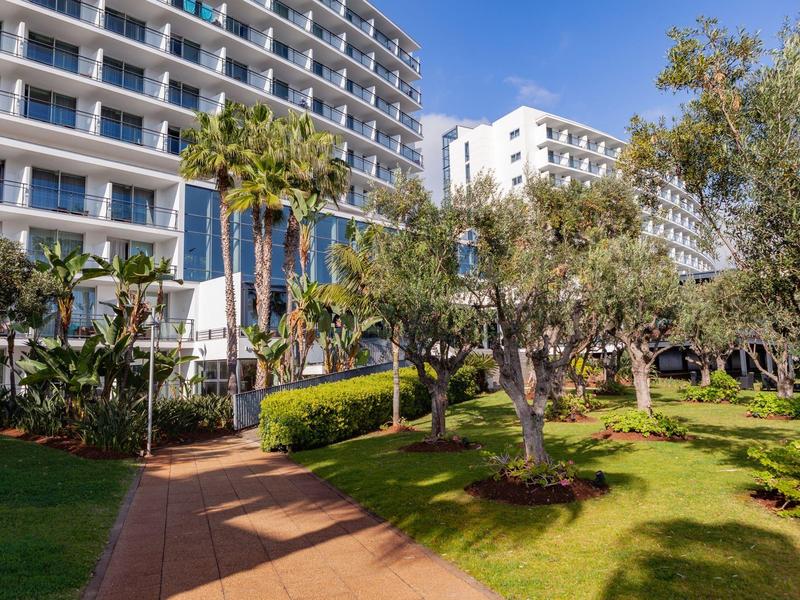 Edificio dell'hotel con balconi e giardino ben curato con alberi e sentiero lastricato.