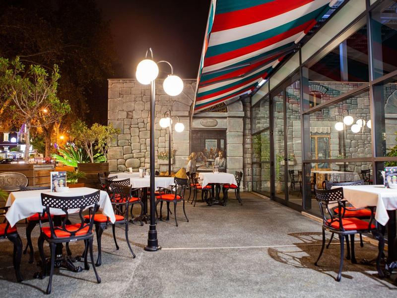 Terrazza esterna dell'hotel illuminata con tavoli apparecchiati e sedie di notte.