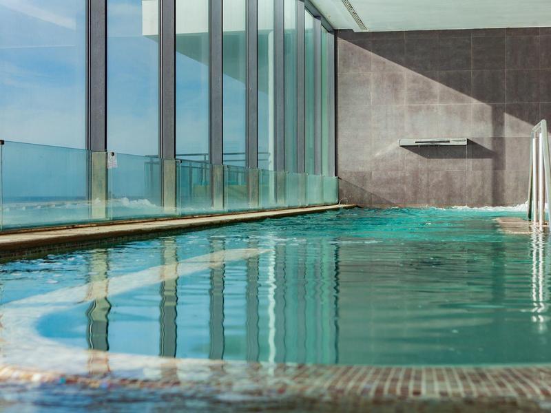Piscina interna con grandi finestre e vista sul mare in un hotel moderno.