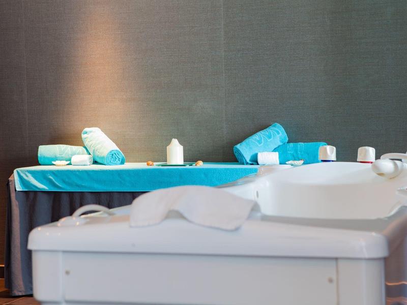 Sala benessere ben illuminata con due lettini da massaggio e asciugamani blu posizionati sopra.