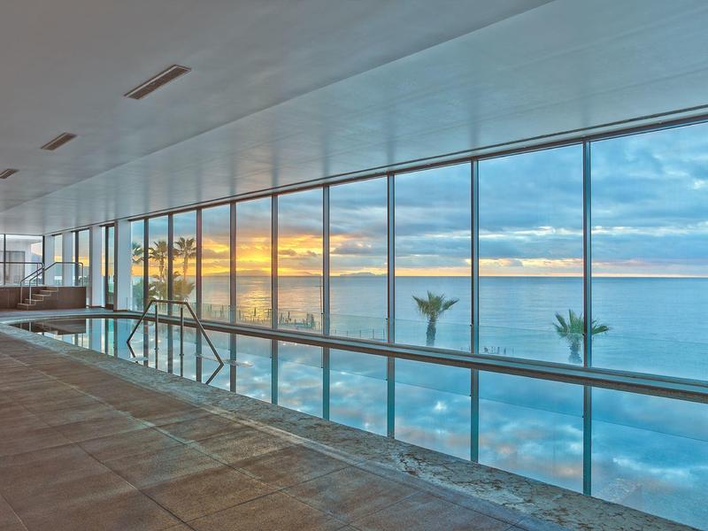 Grande stanza con finestre dal pavimento al soffitto che si affacciano sul mare al tramonto.