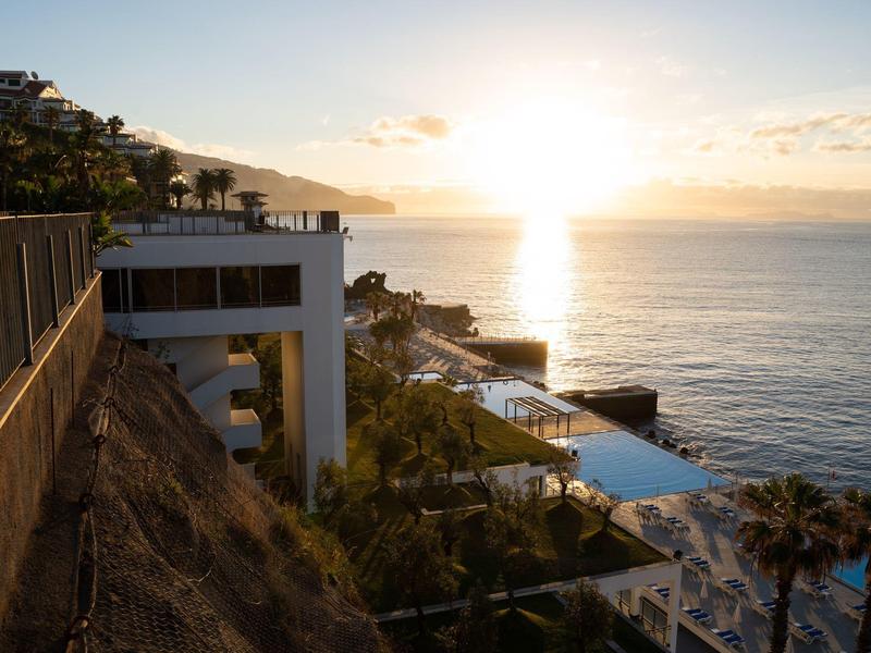 Tramonto sulla costa con edifici dell'hotel, piscina e palme sulla collina.