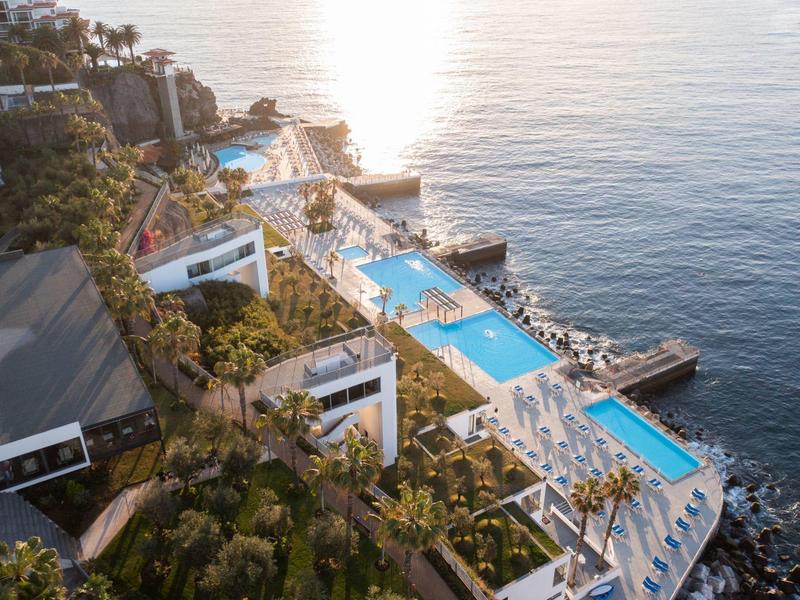 Hotel di lusso con più piscine su una scogliera che domina il mare al tramonto.