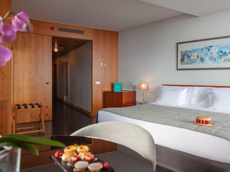 Camera d'albergo moderna con grande letto, tavolo e decorazioni con fiori e snack.